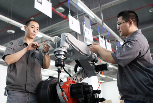 Two technicians adjust a robot at a high-tech enterprise in Chongqing. (Photo: Chen Shichuang/For China Daily)
