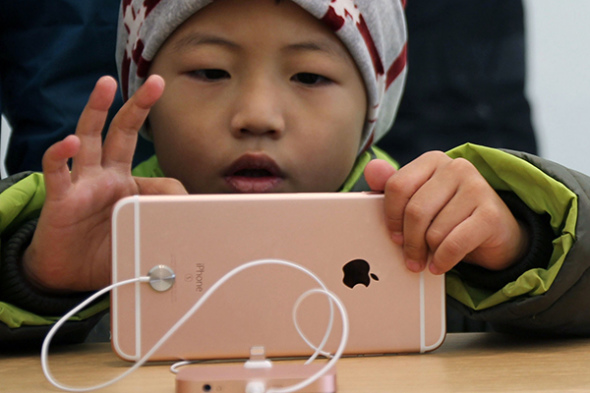 A boy plays with a smartphone in an outlet of Apple Inc in Qingdao, Shandong province. 