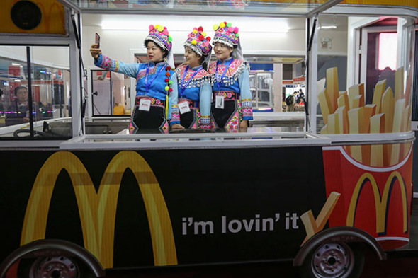 Ethnic Yi girls in traditional outfits take photographs at a McDonald's mobile dining carriage during a tourism expo in Beijing on Friday.(Feng Yongbin/China Daily)