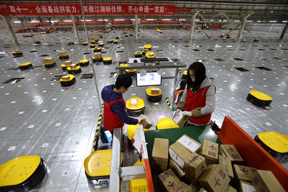 Staff work alongside robots to help sort out packages at a logistics company in Tianjin. (ZHU XINGXIN/CHINA DAILY)