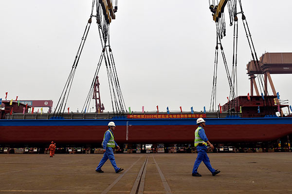 Two technicians pass by the world's first 2,000-metric-ton all-electric cargo ship during its debut in Guangzhou, capital city of Guangdong province. The ship can run 80 kilometers after being fully charged. (Photo/China Daily)