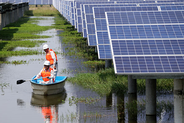 Two electricians paddle through a fishery where a photovoltaic power station was set up, in Jiangling county, Hubei province. (Zhou Guoqiang / For China Daily)