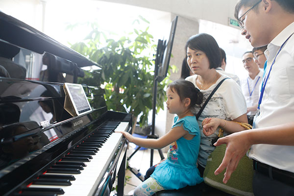 A girl and her mother experience an artificial intelligence piano produced by Guangzhou Pearl River Piano Group Co Ltd during a recent AI forum held in Guangzhou, Guangdong province.(Photo by Tan Qingju/China Daily)