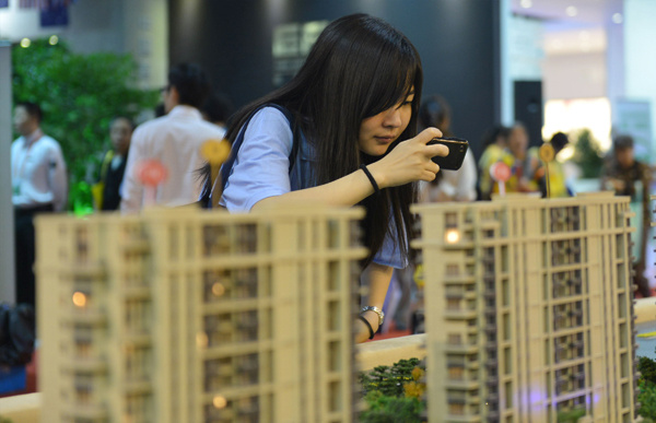 A Hangzhou denizen takes pictures of models of a housing estate at a sales center. China's prominent property firms are entering the long-term home lease market, in line with government policy. (Photo provided to China Daily)