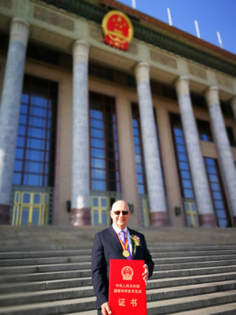 Phil Coates with his award certificate in front of the Great Hall of the People in Beijing on Monday. (Photo provided to China Daily)