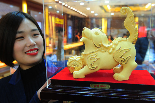 An employee of a jewelry shop in Fuyang, Anhui province, displays a dog statue made of gold. (Photo/China Daily)