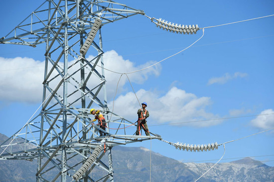 An employee connects electrical cables atop a 30-meter-high, 110 kV power transmission tower in the Tibet autonomous region. State Grid Corp of China, the country's largest grid operator, will further push for a unified national electricity market. (Photo by Song Weixing/For China Daily)