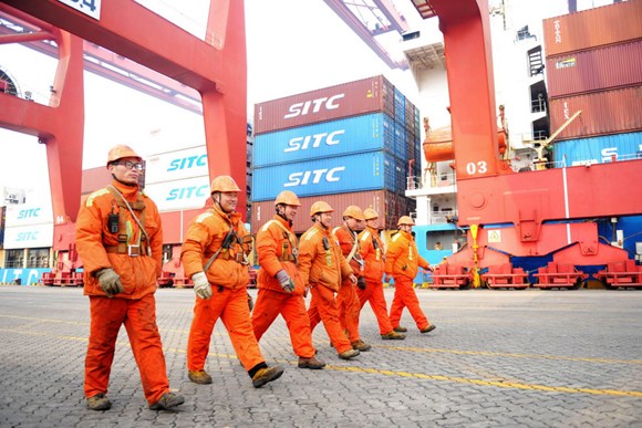 Workers walk past containers at Qingdao Port, Shandong province. (Photo by Yu Fangping/For China Daily)