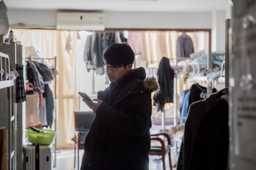 A tenant in a Beijing apartment checks his smartphone for leads to cheaper accommodation. (Photo provided to China Daily)