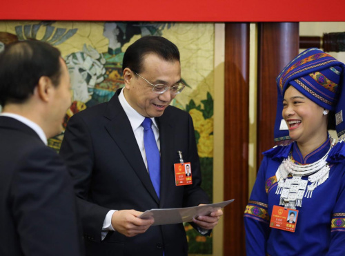 Premier Li Keqiang examines photos presented by Wei Zhaohui, a deputy from the Guangxi Zhuang autonomous region (right), on Tuesday. The photos show major changes in Weis home village. Li joined a group discussion with the delegation. (Photo/China Daily)