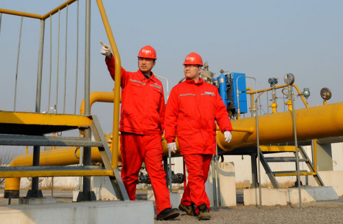 Two employees of Sinopec walk past a gas pipeline of the company in Puyang, Henan Province. (Photo by Hu Qingming/For China Daily)