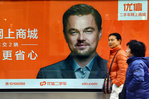 Pedestrians pass by a poster of Youxin, an online used car dealer, on a Beijing street on March 9. The poster featuring Hollywood icon Leonardo DiCaprio publicizes Youxin's online shopping mall. (Photo by Ma Jian/for China Daily)