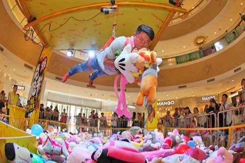 To popularise claw doll grabber machines, reality games are enacted at malls to demonstrate the fun. At the Joy City shopping mall in Yantai, Shandong province, a consumer, suspended by a crane mechanism, doubles up as a doll grabber. (Photo by Tang Ke/For China Daily)