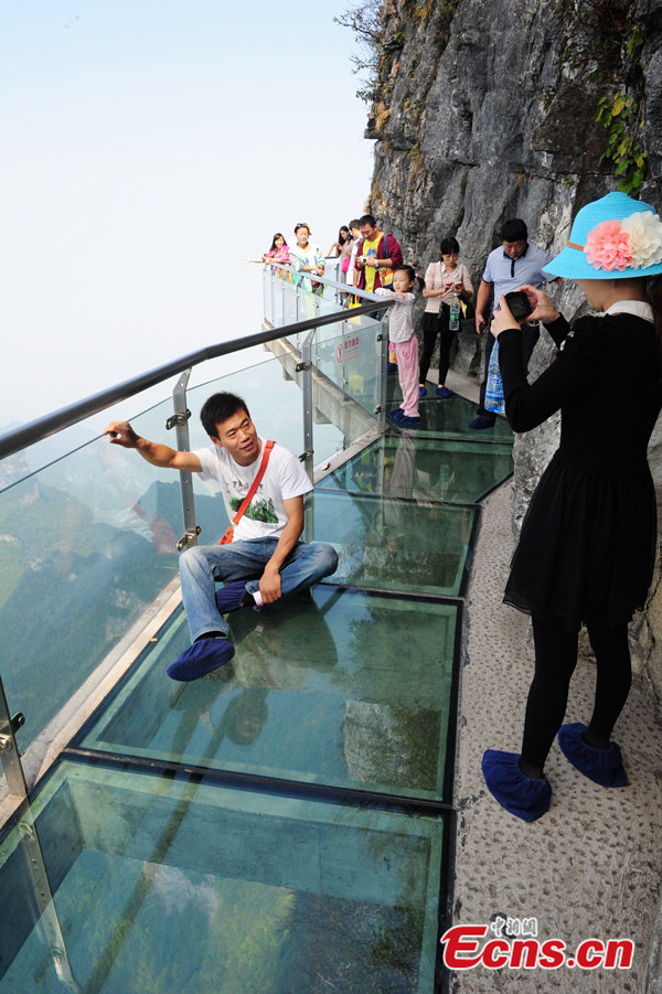 A visitor poses for photos on a glass plank road at Tianmenshan National Forest Park of Zhangjiajie in Hunan province on October 13, 2013. The glass plank road is about 60 meters long and 1430 meters above the sea level. [Photo: China News Service / Yang Huafeng]