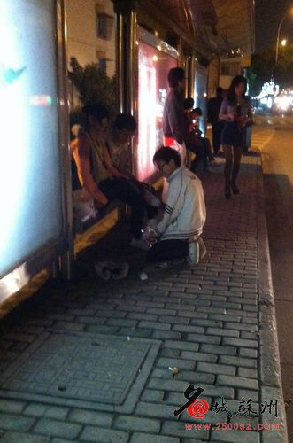 A boy kneeling down in front of a girl wearing a ponytail about the same age, at a bus stop in Wuzhong district.