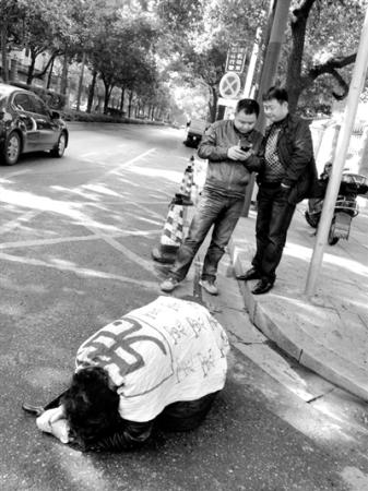 In another photo taken the same day, Duan kneels down on the street, wrapped in a piece of white cloth bearing the word Yuan (injustice). A meter away, two officials play with a mobile phone.