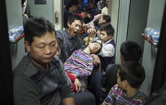 Numbers of passengers sit on the floor of aisle on the train, because their tickets are seatless.