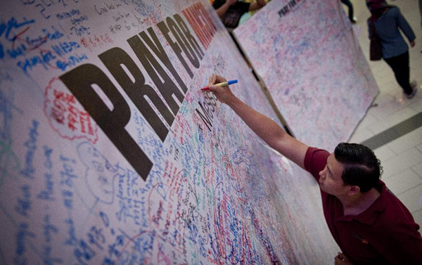 A civilian writes down his well wishes for the missing aircraft on a wish wall in a market in Kuala Lumpur, Malaysia, March 16, 2014. (Photo/Xinhua)