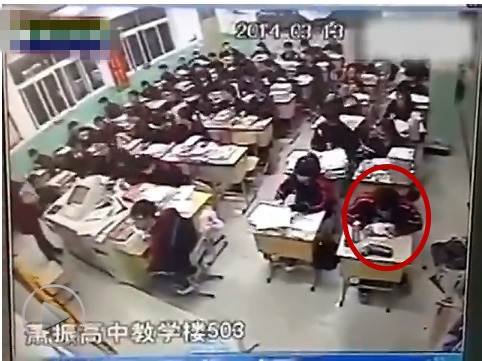 The boy sits motionless in the first row by a window. [Screenshot of video]