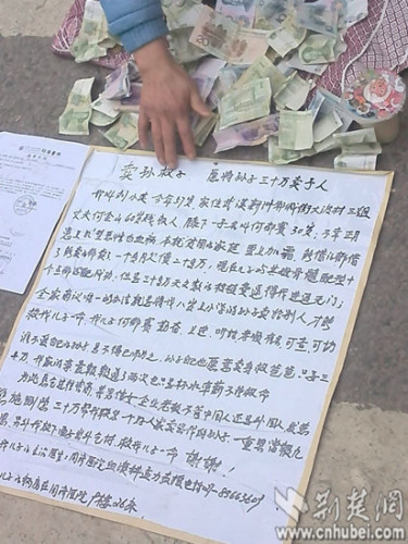 The poster in front of Liu reads she wants to trade her grandson for 30,000 yuan to save her son. (Photo: cnhubei.com)