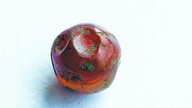 A tiny perforated bead around 0.3 centimeters in diameter is discovered at the Great Hinggan Mountain cave. (Photo: Guangming Daily)
