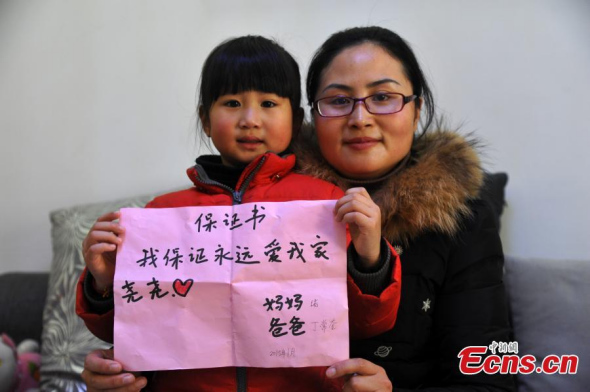 A woman and her first daughter pose with a written promise about having the second child in their family in Hefei, East Chinas Anhui province, Feb 2, 2015.  (Photo: China News Service/Han Suyuan)