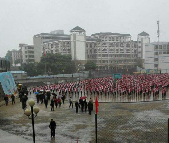 Sudents at at No. 1 Middle School in Rongzhou town perform exercises in the rain while visitors walk around with umbrellas on March 13. (Photo/China Youth Daily) 