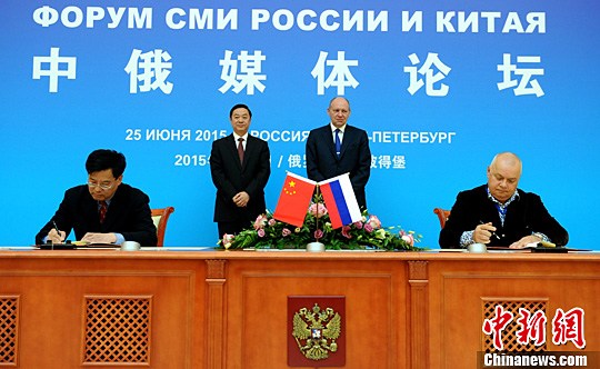 China News Service (CNS) President Zhang Xinxin (L, 1st)and Dmitry Kiselev(R, 1st), head of the Russia Today international news agency, sign a cooperation deal on the sidelines of the China-Russia Media Forum in St Petersburg on Thursday. (Photo/China News Service)