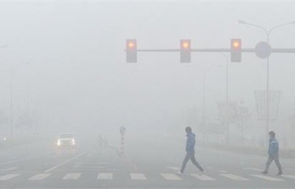 People walk across an intersection during a smoggy day. (File photo)