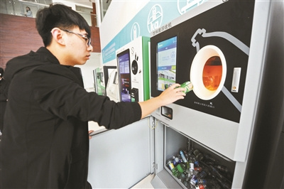 A young man puts a waste bottle into a recycling container in Beijing. (Photo/Beijing Youth Daily)