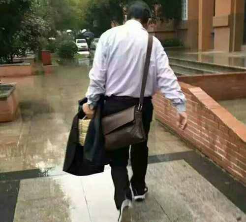 Shi Danlin, 67, an old professor at Wuhan University of Science and Technology, protects student exercise books from rain with his suit. (Photo from Weibo) 