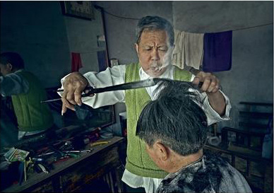 Wang Weimei, a barber, uses burning tongs to perm hair for his customers. (Photo/Chengdu Business Daily)