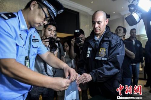 A Chinese police officer hands over a U.S. fugitive's personal belongs to the U.S. police. (File photo/China News Service)