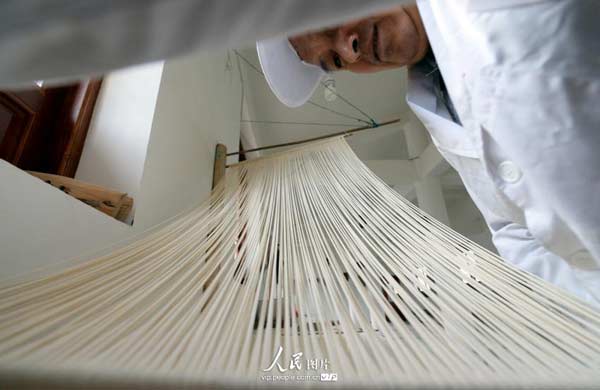 Pulling one bamboo stick from the other, the noodles are stretched. [Photo/People's Daily Online] 