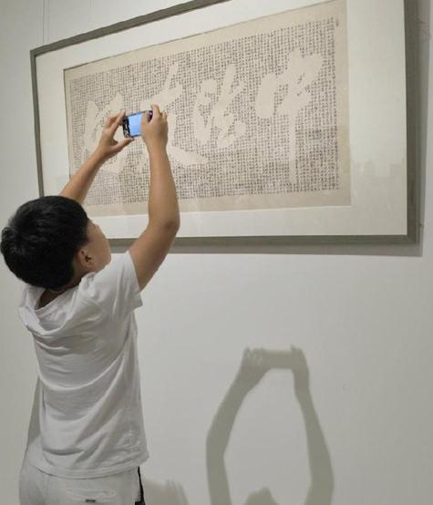 A little boy takes a picture of Sino-French Friendship, a calligraphy work by Chinese calligrapher Lin Senhe at the exhibition in the National Museum in Beijing, August 5, 2014. [Photo/Xinhua]