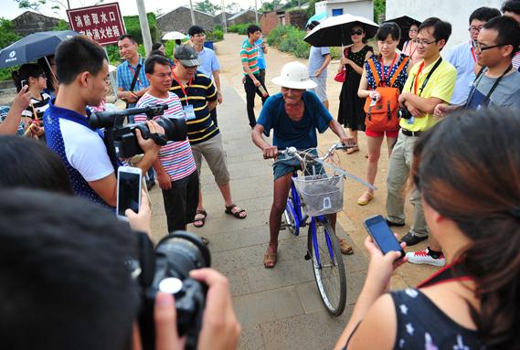 A 99-year-old man form the village rides a bike and is surrounded by visitors, in Luoyi village, Chengmai county of Hainan province, Sept 22, 2014. [Photo provided to chinadaily.com.cn]