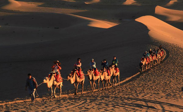 Tourists riding on camels visit the scenic spot of the Mingsha Mountain in Dunhuang city, Northwest China's Gansu province, July 13, 2014. Dunhuang ranked seventh among the 30 most beautiful counties in China for the year 2014 released by China Institute of City Competitiveness. [Photo/Xinhua]  