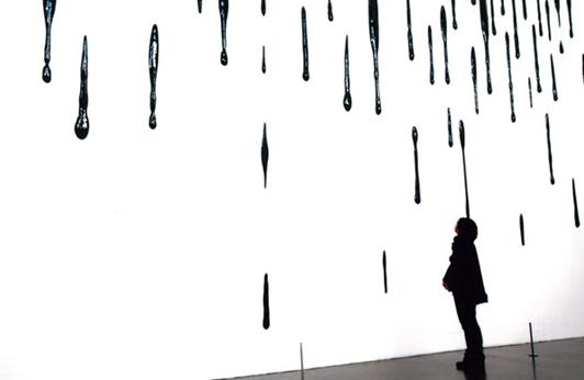 A visitor views artist Liu Jianhua's installation series Trace, which features porcelain drops on a wall.(Photo provided to China Daily)