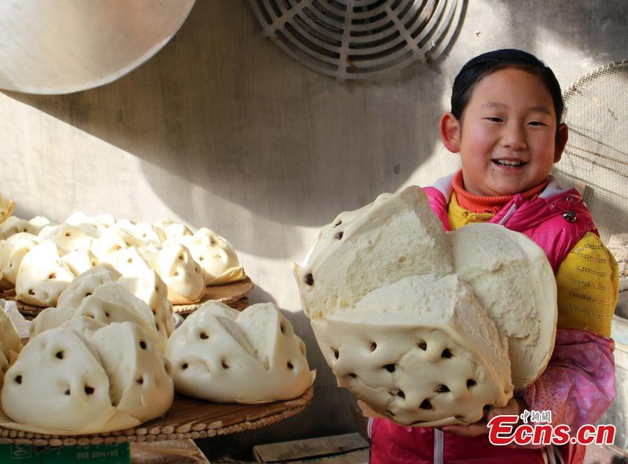 A child shows a steamed bun stuffed with dates in Weihai, East China’s Shandong province, Feb 5, 2015. Local people have the tradition to make steamed buns with high-quality wheat flour, peanut oil, white sugar, eggs, and fresh milk before the Spring Festival, China’s Lunar New Year. The making of steamed buns reminds people of the process of becoming more and more prosperous. [Photo: China News Service/Liu Changyong]
