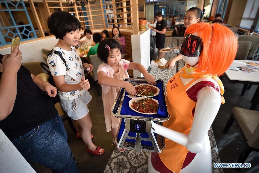 A girl takes dishes delivered by the robot waiter in Haikou, capital of south China\'s Hainan Province, Aug. 3, 2015. A robot waiter was introduced to a restaurant in Haikou. (Photo: Xinhua/Guo Cheng)