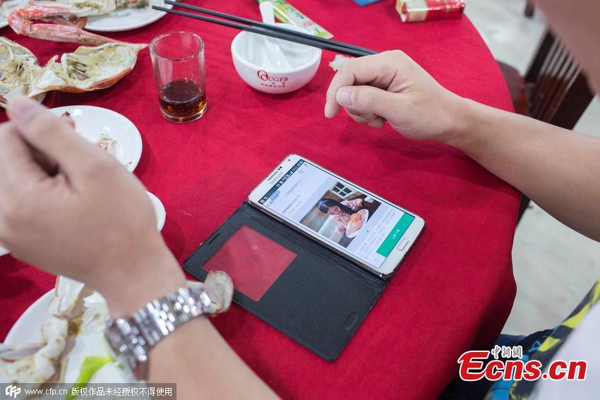 A man comments on a crab-eating service he has ordered online at a seafood restaurant in Hangzhou, East China’s Zhejiang province, Aug 28, 2015. The woman, 27, is a retired airline stewardess and known online for her crab-eating skills, such as separating the legs and claws to get meat. She offers the service on Taobao.com, China’s largest e-commerce site, and charges 10 yuan ($1.6) to prepare crab meat and five yuan extra to help with eating. The man spent 260 yuan on the service. (Photo/CFP)