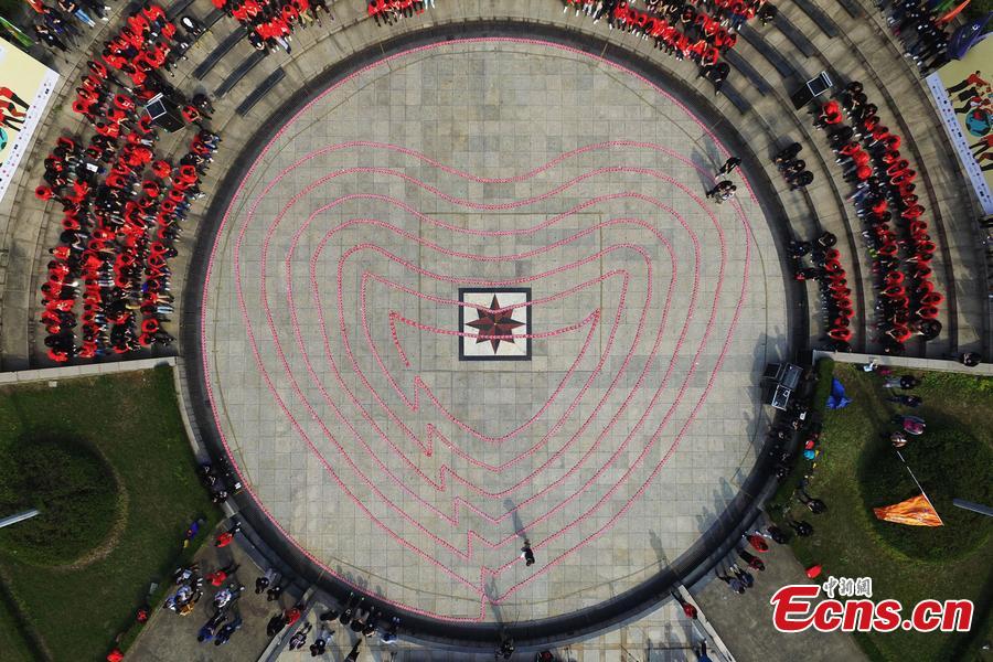 Students and charity workers display envelopes containing prayer cards in a heart shape in Zhejiang Chinese Medicine University in Hangzhou, East China\'s Zhejiang province, on Monday. The event, to raise funds for students in poverty-stricken areas of China, will see the envelopes posted to students and volunteers to pass on the spirit of charity. The envelop chain, reaching 335.23 meters in length, set a new Guinness World Record for the longest envelope chain. (Photo/CFP)