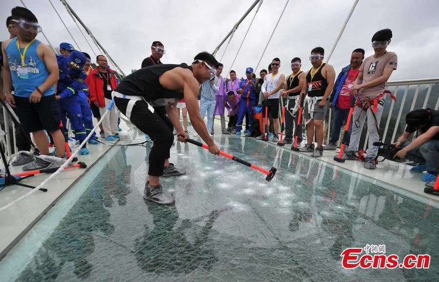 A visitor strikes the glass-bottomed bridge with a hammer for a safety test at Zhangjiajie Grand Canyon on June 25, 2016 in Zhangjiajie, Hunan Province of China. The bridge is 430 meters long, six meters wide and 300 meters above the valley. (Photo: China News Service/ Yang Huafeng)