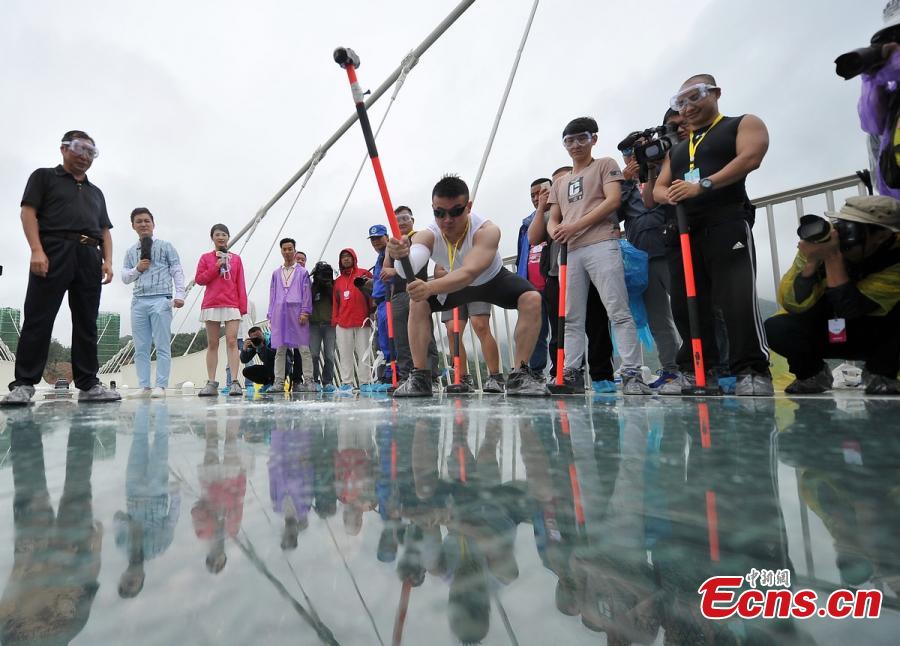 A visitor strikes the glass-bottomed bridge with a hammer for a safety test at Zhangjiajie Grand Canyon on June 25, 2016 in Zhangjiajie, Hunan Province of China. The bridge is 430 meters long, six meters wide and 300 meters above the valley. (Photo: China News Service/ Yang Huafeng)