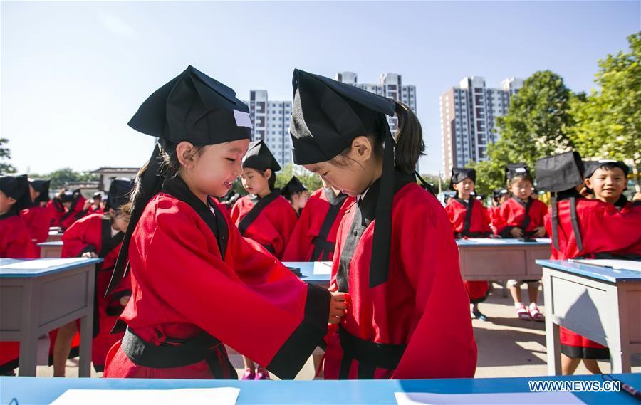 Two children arrange hat and clothes of each other at the first writing ceremony in Zhixing Elementary School in Qiaoxi District under Xingtai, north China\'s Hebei Province, Aug. 31, 2016. More than 200 children wearing Han-style costume, or Hanfu attended the ceremony, a traditional education activity for children to start their school life in China, in Xingtai Wednesday. (Photo/Xinhua)