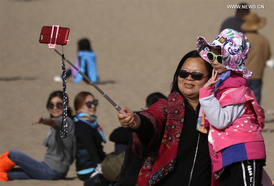 Tourists pose for photos at the Mingsha Sand Mountain scenery zone in Dunhuang, northwest China\'s Gansu Province, south China\'s Guangxi Zhuang Autonomous Region, Oct. 2, 2017. China witnessed more than 710 million tourist trips during the eight-day National Day and Mid-Autumn holidays, ringing up to about 590 billion yuan (88.68 billion U.S. dollars) in tourism income, according to the National Tourism Administration. (Xinhua/Zhang Xiaoliang)
