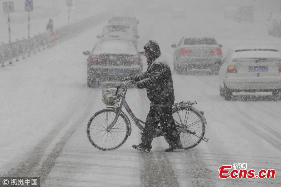 Pedestrians walk amid snowfall in Yantai, east China\'s Shandong Province, Dec. 11, 2017. A cold wave brought a heavy snowfall here.(Photo/VCG)