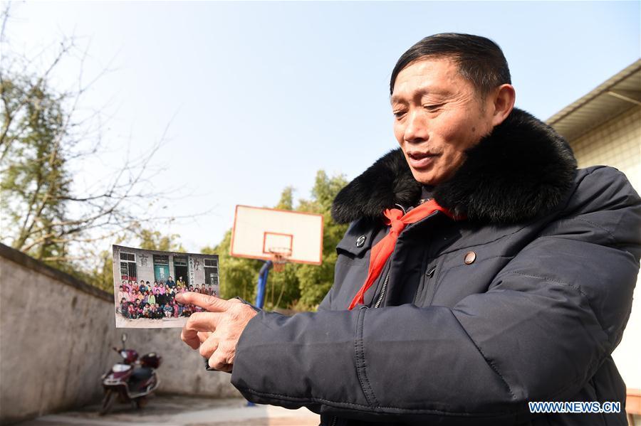 Tan Zeguang shows a photo of his former students at the Gaoshan Village Primary School in Tonggu Township of southwest China\'s Chongqing Municipality, Jan. 8, 2018. Tan Zeguang, a rural teacher of Gaoshan Village Primary School, has been teaching students in this remote area for a total of 40 years. Tan has to take care of both courses and daily life of students when they are at school, which is more than five kilometers away from the nearest town. In the past 40 years, more than 500 children were ever taught by Tan. As more students choose to attend better schools in towns, the school in which Tan stays has fewer students. But Tan still sticks to his post despite reaching retirement age. To his comfort, two young teachers have come to teach at the school and will continue his teaching career. (Xinhua/Tang Yi)