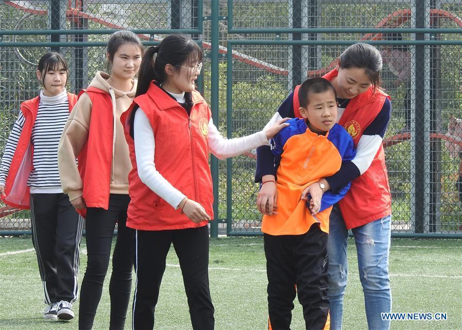 Volunteers stay with an autistic child on the football field at Xinnan Community in Lianyungang City, east China\'s Jiangsu Province, April 1, 2018. A football team, composed of 22 autistic children aging from 7 to 16, was jointly set up by the community and an autism care center ahead of the World Autism Awareness Day, which falls on April 2 every year. The football team will have trainings and games every week. (Xinhua/Geng Yuhe)