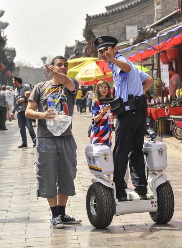A police officer gives directions to a tourist as he patrols a street on a Segway-like self-balancing scooter in the Pingyao Ancient City, a popular tourist destination, in Jinzhong, north China\'s Shanxi Province, May 13, 2018. (Xinhua/Liang Shengren)